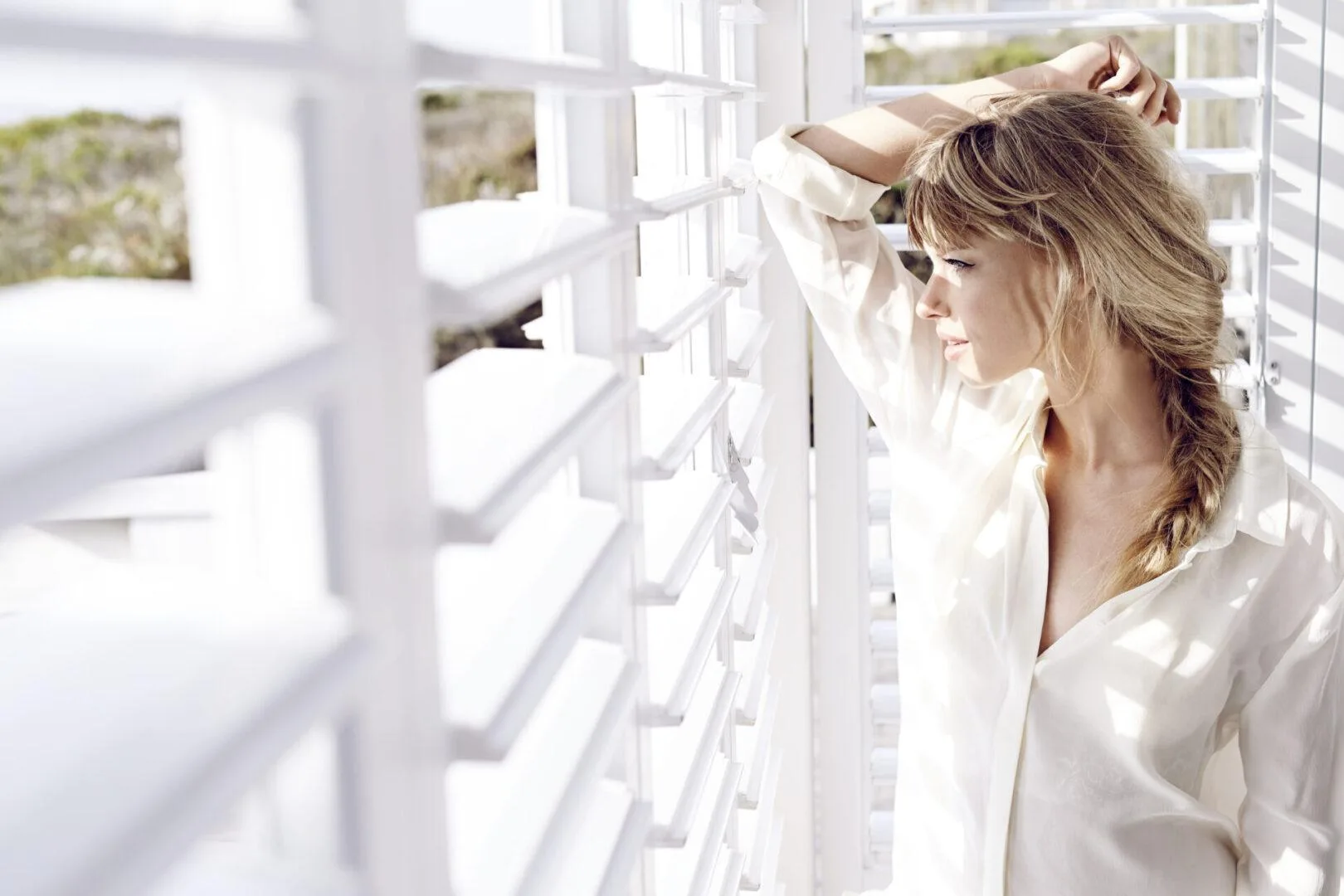 Woman opening white plantation shutters by a bright window