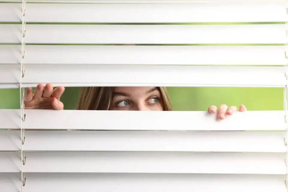 Woman peeking through white 2-inch faux wood blinds