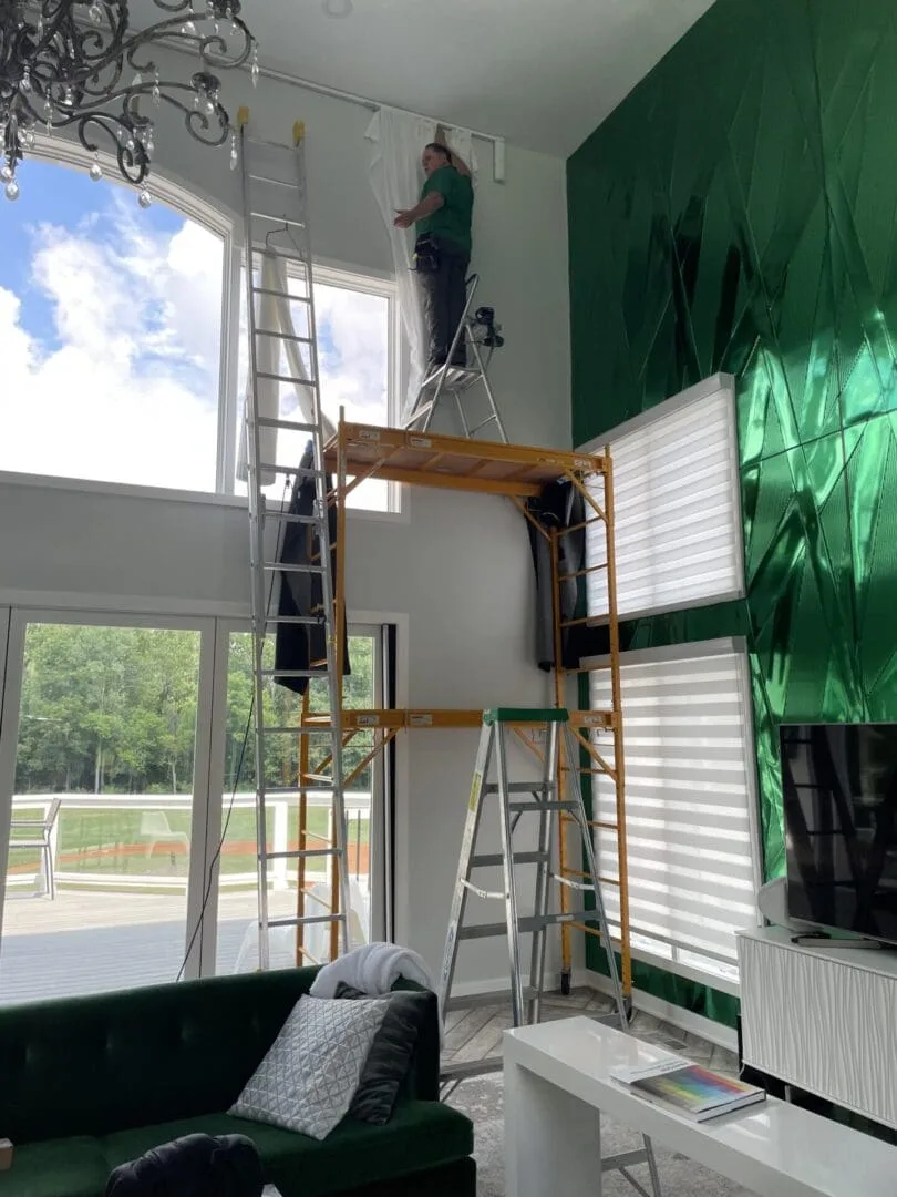 Shutter King USA installer on a ladder hanging drapery hardware in an Indianapolis home
