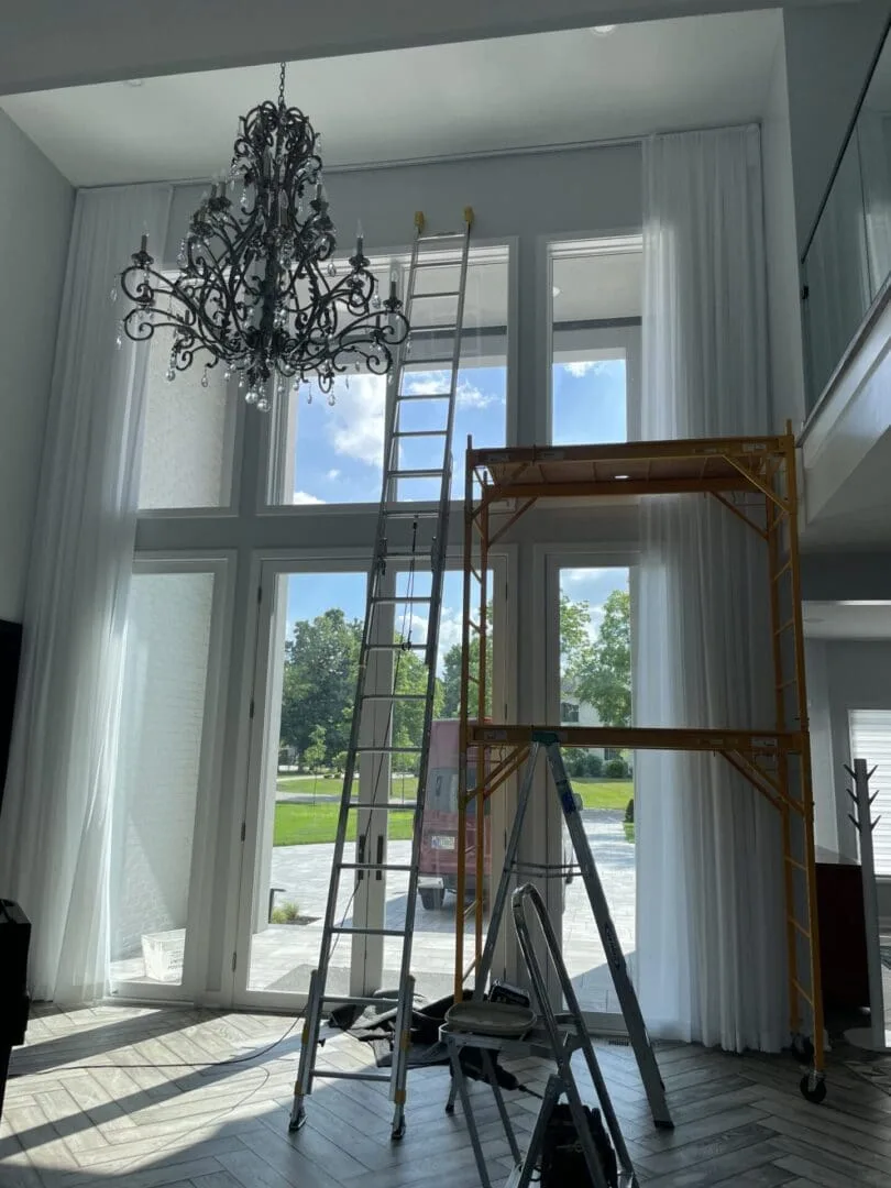 Ladder set up under a chandelier to install drapery on tall Indianapolis windows