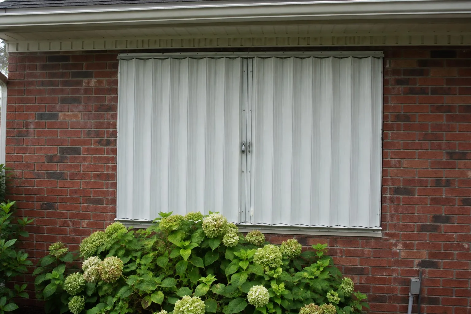 Closed white accordion hurricane shutter protecting a window on a brick Indianapolis home