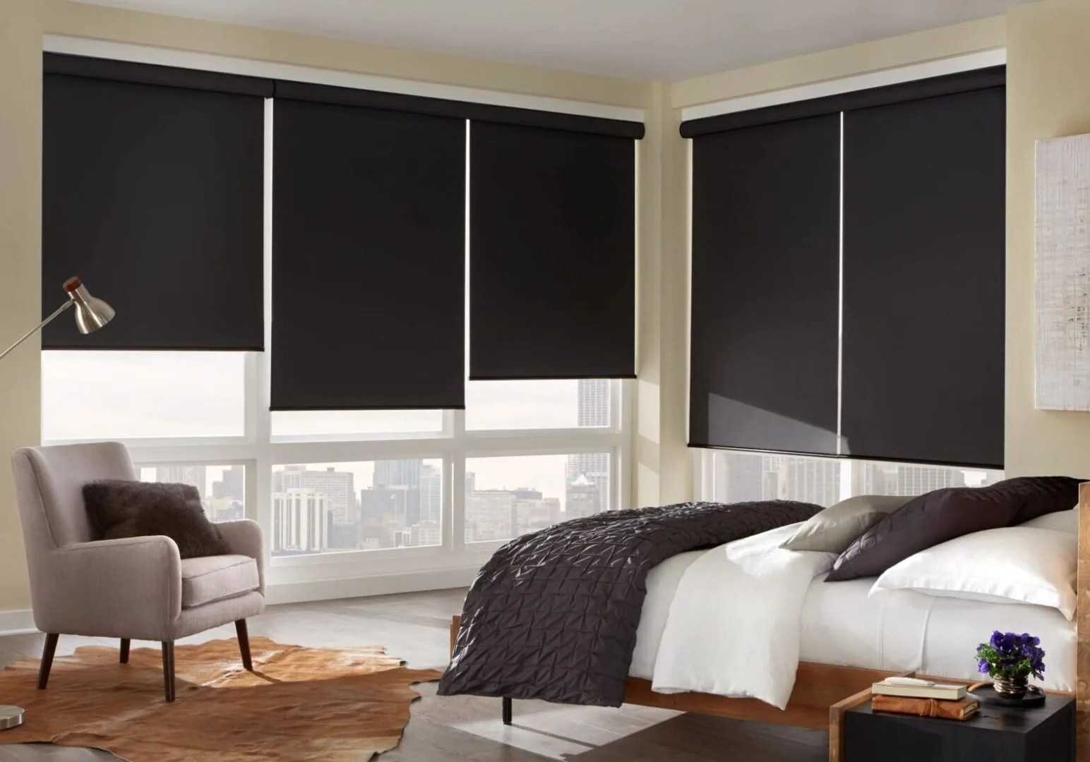 A bedroom with black roller shades and white comforter.
