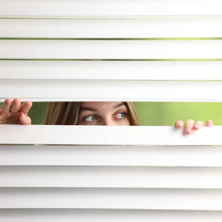 Woman looking through white 2-inch faux wood builder blinds in an Indianapolis home