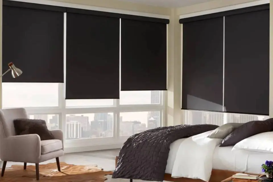 A bedroom with black roller shades and white walls.